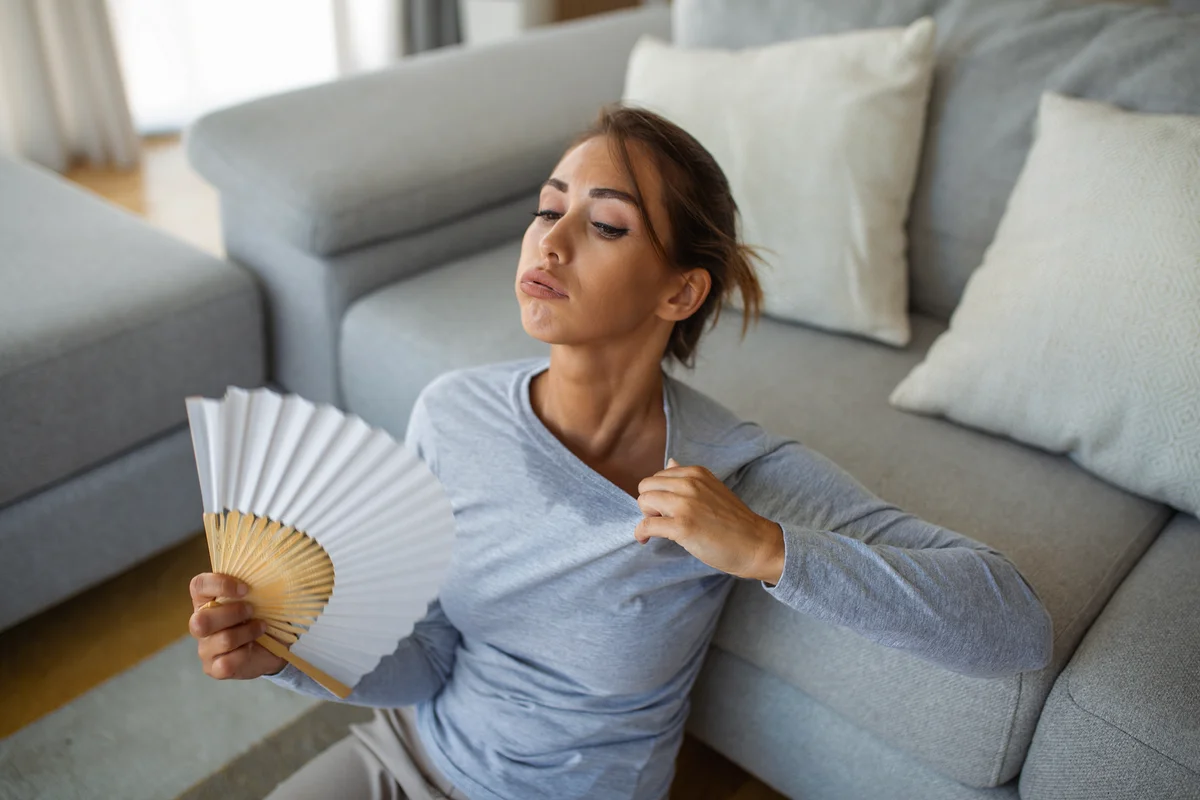 Woman fanning herself while sitting on the floor, experiencing a hot flash
